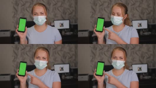 一名戴着医用口罩的妇女在家中手持一部绿色屏幕的手机。高清在线视频素材下载