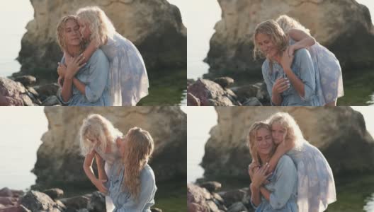 快乐的金发妈妈和可爱的女儿一起在日出的海滩上散步高清在线视频素材下载