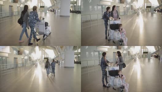 一名妇女带着两个女儿拉着一辆手提行李车沿着机场大厅走。乘客在等候区。高清在线视频素材下载