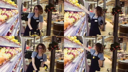 侧面的漂亮的白人工人在黑色围裙和手套stocking在超市的水果。年轻员工在工作。卷曲的女性排列水果在架子上高清在线视频素材下载