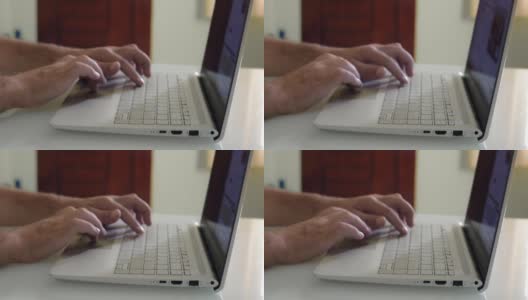 一个男人的手在一个笔记本电脑键盘上打字的特写，在一个家庭办公室的桌子上。高清在线视频素材下载