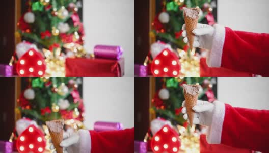 圣诞老人在家里的圣诞装饰前举起一个冰淇淋蛋筒，咬上几口高清在线视频素材下载