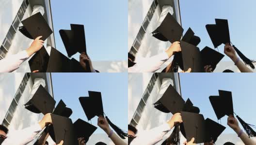 快乐的学生们穿着长袍在空中展示着学位帽。教育、毕业与人观念。高清在线视频素材下载