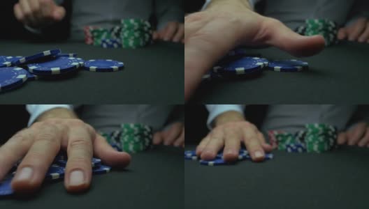 在黑色背景下，男人的手从扑克桌上拿走筹码。筹码和手放在绿色桌上。“手”用慢动作拿走扑克中的赢钱高清在线视频素材下载