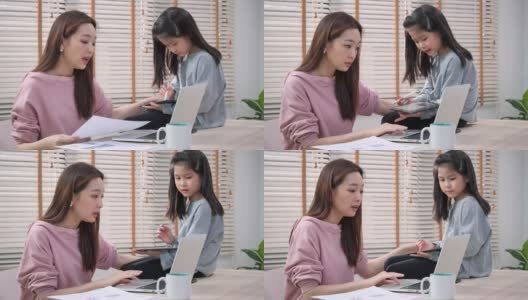 一个亚洲家庭，女商人在工作，小女孩坐在家里的桌子上。母女二人在家中被隔离的时候，在网上开会，开心的表情。高清在线视频素材下载