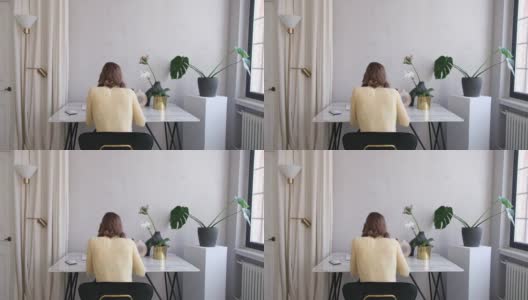 穿着马球衫的女人坐在桌子旁，房间里有郁郁葱葱的室内植物高清在线视频素材下载