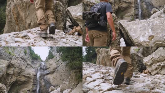 一个人在山上攀登岩石，看到了上游的瀑布。靴子在陡峭的岩石上行走的低角度视图。徒步者在户外徒步行走的脚步。在岩石地形上行走。高清在线视频素材下载