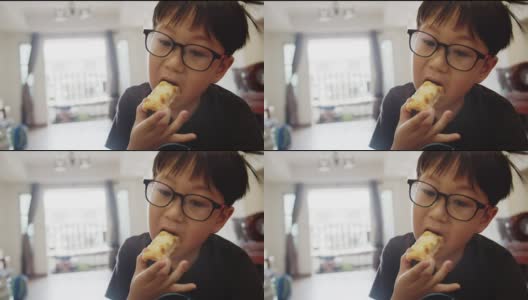 可爱可爱的亚洲孩子，戴眼镜的男孩喜欢在家里吃面包条高清在线视频素材下载
