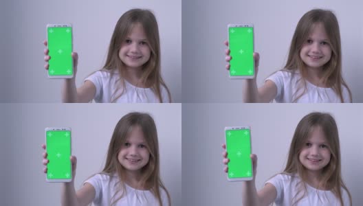 可爱的小女孩用绿色的屏幕展示手机，模拟手机，手机。绿屏智能手机的色度键设置为广告。科技、小玩意和孩子。儿童应用演示高清在线视频素材下载