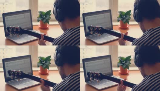 戴着耳机的男人在窗前用笔记本电脑弹着电吉他高清在线视频素材下载