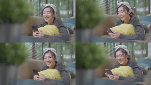 幸福快乐微笑年轻的成年亚洲女性女人穿着黄色的布手在智能手机交谈在家里的沙发远程隔离锁定时期家内部背景高清在线视频素材下载