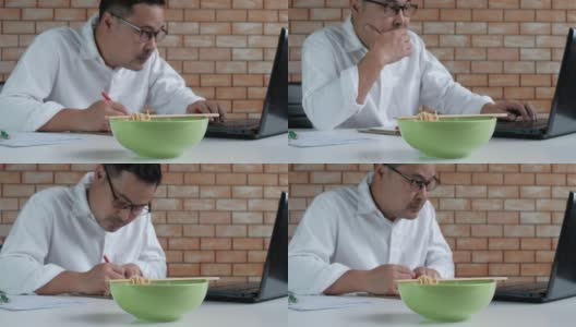 亚洲男性忙于工作，午餐时间在办公室吃方便面。高清在线视频素材下载