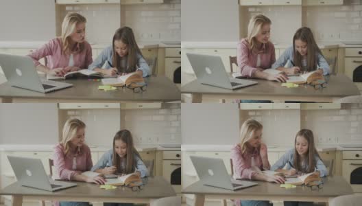 一名女子微笑着在餐厅用笔记本电脑帮助年轻女孩做作业高清在线视频素材下载