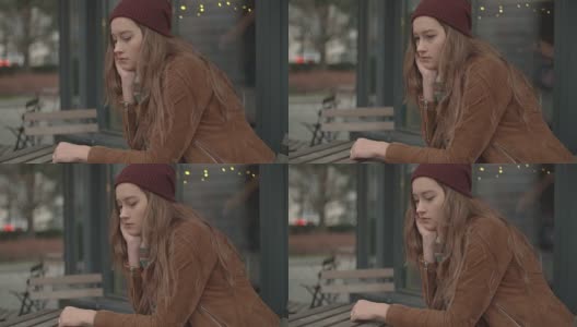 一个忧郁的白人女孩坐在露天咖啡馆里。高清在线视频素材下载