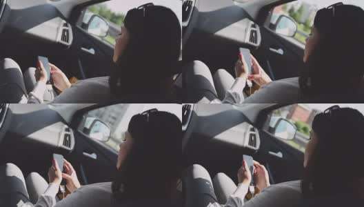 年轻的黑发女孩坐在驾驶座上。利用手机。夏天阳光灿烂的日子高清在线视频素材下载