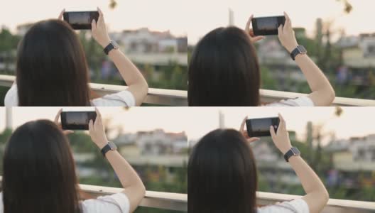 年轻女孩使用智能手机拍摄城市照片的特写，而一个美丽的日落。高清在线视频素材下载