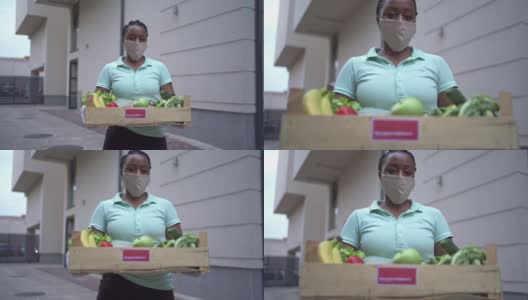 黑人女性志愿者在冠状病毒大流行期间，拿着装着新鲜蔬菜的板条箱，为需要的人运送高清在线视频素材下载