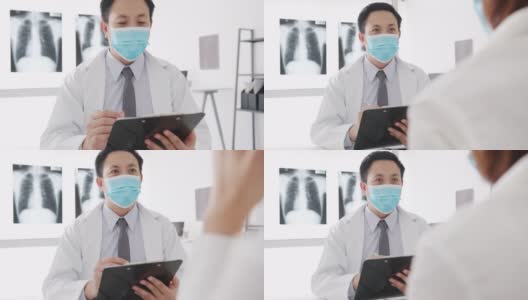 严重的亚洲男医生戴着防护口罩，用剪贴板与女病人在医院的办公室里传递好消息，谈论结果或症状。高清在线视频素材下载