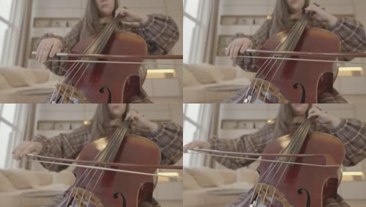 年轻女子音乐家与弓在家中演奏大提琴室内高清在线视频素材下载