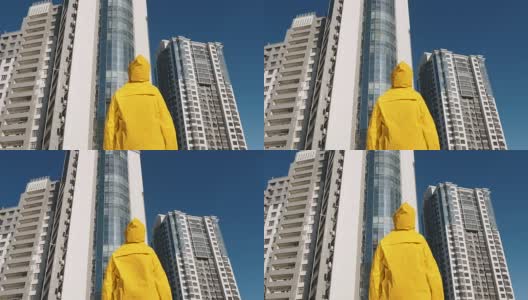 一个穿着黄色雨衣的人站在现代住宅区大楼前高清在线视频素材下载