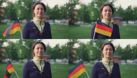 慢动作肖像欢快的年轻女子挥舞官方德国国旗，看着镜头，而站在美丽的树木和草坪的美丽的绿色公园。高清在线视频素材下载