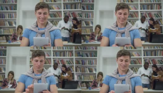 可爱的整洁开朗的现代家伙坐在大学图书馆里，用i-pad搜索需要的信息来完成家庭任务高清在线视频素材下载