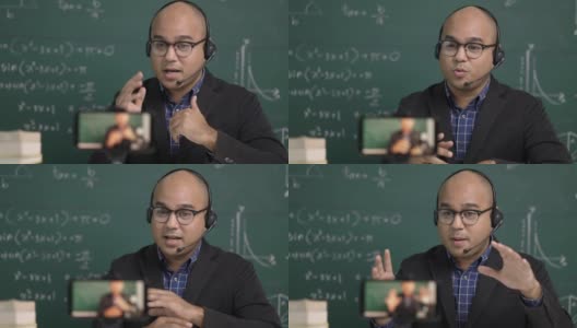 印度年轻教师男子戴着耳机坐着通过智能手机进行在线视频会议直播。亚洲数学教师在线授课，供学生在线学习。高清在线视频素材下载
