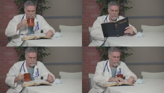 一位成熟的内科医生在医院休息室里，一边喝咖啡，一边读着他的圣经。高清在线视频素材下载