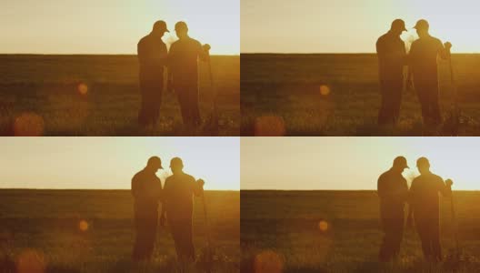 两个农民在地里聊天，用着药片。美丽的夕阳，两个男人的剪影。Copyspace组成高清在线视频素材下载