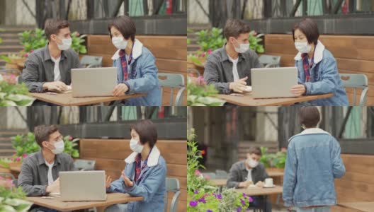 一名年轻的亚洲女性在户外咖啡馆的餐桌上与男同事会面，并在笔记本电脑上向他展示项目想法，两人都戴着医用口罩高清在线视频素材下载