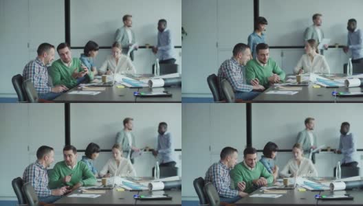 在办公室会议室工作的各类商务人员的跟踪拍摄。两个男人在办公桌前讨论文件，女同事在旁边的笔记本上做笔记。两个商人在背后交谈高清在线视频素材下载