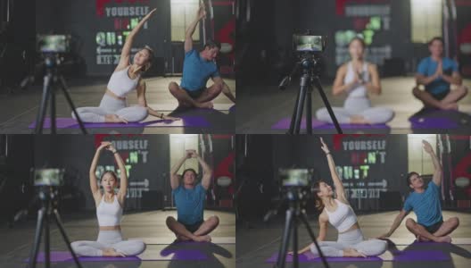 一名亚洲瑜伽女教师在健身房为一名白人男子授课。该女孩在网上直播自己的课程，并通过智能手机录制，以便在COVID - 19疫情期间健身房关闭时将学生隔离在家。高清在线视频素材下载