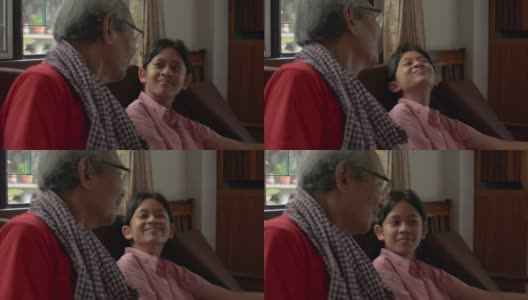 可爱的亚洲少女孙女在客厅里和她白发苍苍的爷爷坐在一起聊天，开心地笑着。家庭中两代人的联系。高清在线视频素材下载