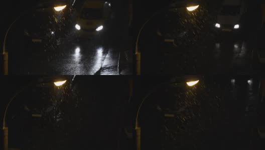 夜间有暴风雪。鸟瞰图。雪在灯下飘落。过往汽车的前灯反射在潮湿的柏油路面上。积雪覆盖在车顶上高清在线视频素材下载