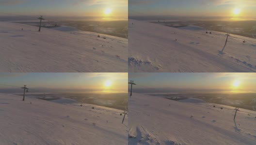 在阳光明媚的冬季日落，人们乘坐缆车在滑雪坡上滑雪和滑板。太阳在坐标系。鸟瞰图。无人机正在横向飞行。远景。高清在线视频素材下载