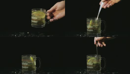男人的手放了一个盛着绿茶的玻璃杯。玻璃杯，里面有有机的干绿茶和柠檬片，在热水中漂浮。缓慢的运动。黑色背景高清在线视频素材下载