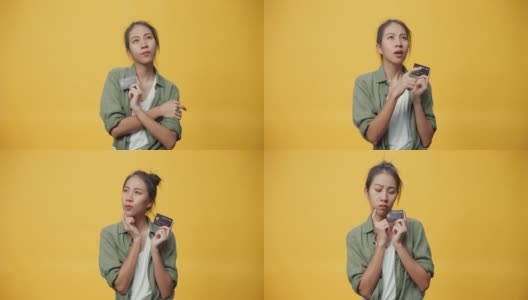 亚洲青年孤立的女士手拿信用卡，带着怀疑的表情侧身看空，黄色背景上带着严肃的脸思考网购。高清在线视频素材下载
