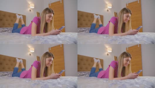 快乐的年轻女子在卧室里用手机发信息。美丽的白色女性，长金发，使用现代手机进行交流和网络。使用智能手机的快乐人群高清在线视频素材下载