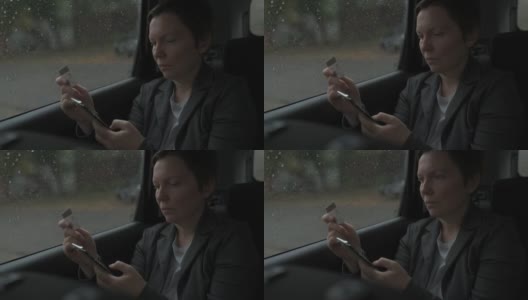 女商人在雨中坐在汽车后座使用信用卡和智能手机进行电子银行高清在线视频素材下载