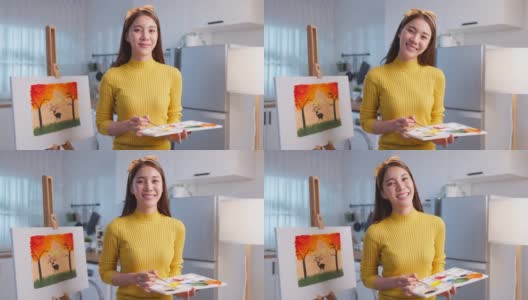 亚洲年轻艺术家女孩在画板上色的肖像在家里。有吸引力的女性绘画艺术图片，创造艺术品与水彩和画笔享受创意活动和看着相机。高清在线视频素材下载