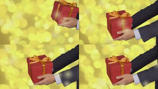 两只男性的手拿着红色的礼盒，上面有金色的蝴蝶结。庆祝除夕礼物礼盒。穿着古典西装的白人。金灯的背景。锁定。高清在线视频素材下载