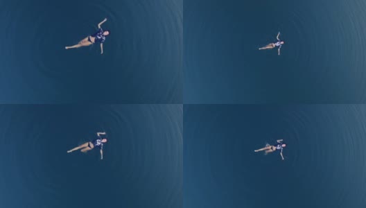 鸟瞰图一个迷人的女孩在黑色t恤漂浮在惊人的蓝色水域高清在线视频素材下载