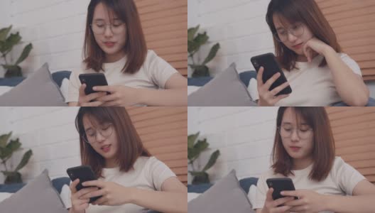 年轻漂亮的亚洲女人坐在沙发上看着智能手机屏幕输入短信聊天高清在线视频素材下载