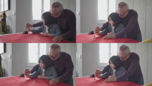 亚洲华人祖父和孙女在中国新年庆祝期间练习书法，家里装饰一张红色的纸高清在线视频素材下载