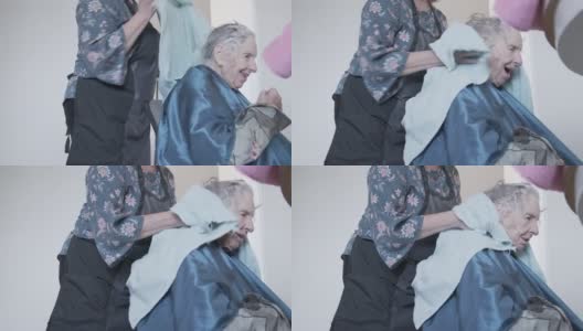 手持拍摄的专业护理发型师干燥一个年长的白人妇女的白色和灰色的头发在厨房里在一个洗发集在家高清在线视频素材下载