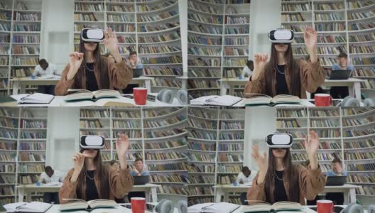 迷人的明亮自信的现代女孩戴着增强现实眼镜坐在图书馆里，在虚拟屏幕上看书的慢动作高清在线视频素材下载