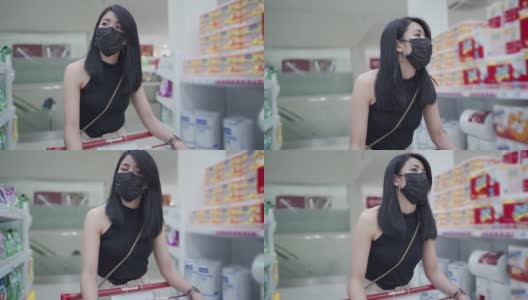 亚洲年轻女性黑色防护面罩推着购物车沿着杂货店通道，妇女在锁定期间得到供应高清在线视频素材下载