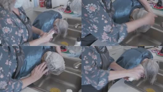 手持拍摄的专业护理发型师洗一个年长的白人妇女的白色和灰色的头发在厨房水槽在洗头设置在家里高清在线视频素材下载