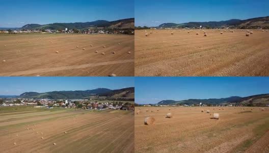 在有圆草堆的田野上空低空飞行。风景如画的小村庄和山峦为背景。高清在线视频素材下载