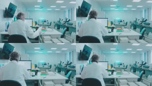 一位上了年纪的医生坐在实验室里，拿着试管，在电脑上工作高清在线视频素材下载
